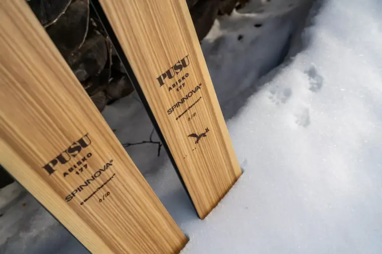 Detailaufnahme der Enden von zwei PUSU Abisko 177 Skiern aus hellem Eschenholz im Schnee. Zu sehen sind die Logos von PUSU, Spinnova und „Moomin Characters“ sowie die Limitierungsnummer „0/50“ und eine kleine Grafik von Sniff.