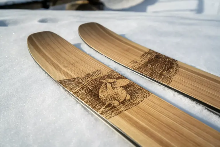 Nahaufnahme der breiten Skispitzen der Abisko Moomin Edition auf einer verschneiten Fläche. Auf dem hellen Holz ist eine eingebrannte Grafik des Mumintrolls zu sehen, der in einer stilisierten Landschaft steht.