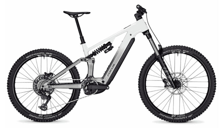 Ein vollgefedertes Focus E-Mountainbike mit einem weiß-grau verlaufenden Rahmen, einem Stahlfederdämpfer und groben Schwalbe Magic Mary-Reifen.